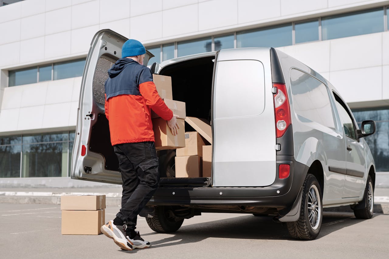 our-story Man in colorful jacket loading cardboard boxes into a van outside an office building.